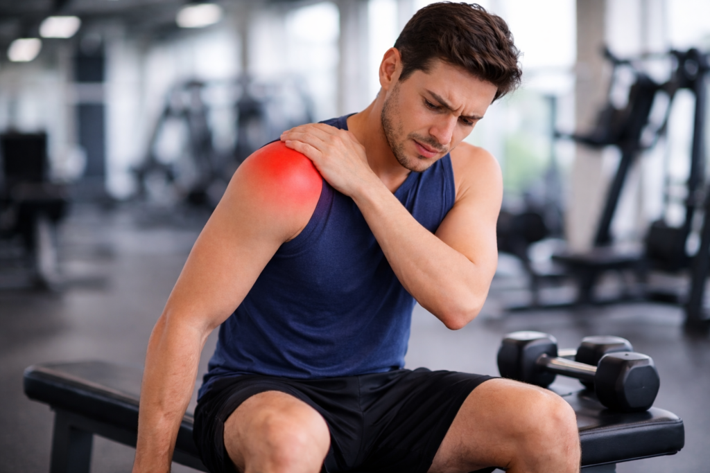 man sitting on gym bench holding shoulder after rotator cuff injury during workout